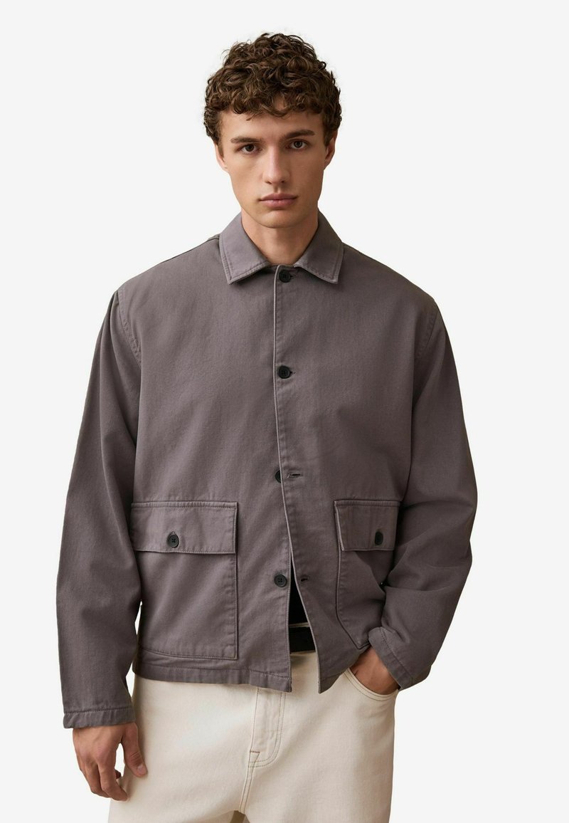 Szara bawełniana kurtka z guzikami z przodu, dwiema przednimi kieszeniami i klasycznym kołnierzem. Materiał ma gładką teksturę i luźny krój.