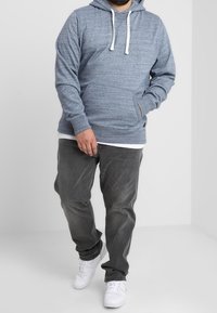 Gray hoodie with white drawstrings, textured fabric, front pouch pocket, paired with gray jeans and white sneakers. Simple design.
