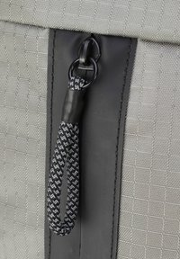Tessuto grigio intrecciato con un motivo testurizzato, dotato di una cerniera in plastica nera e di un tirante intrecciato nero e grigio con un anello.