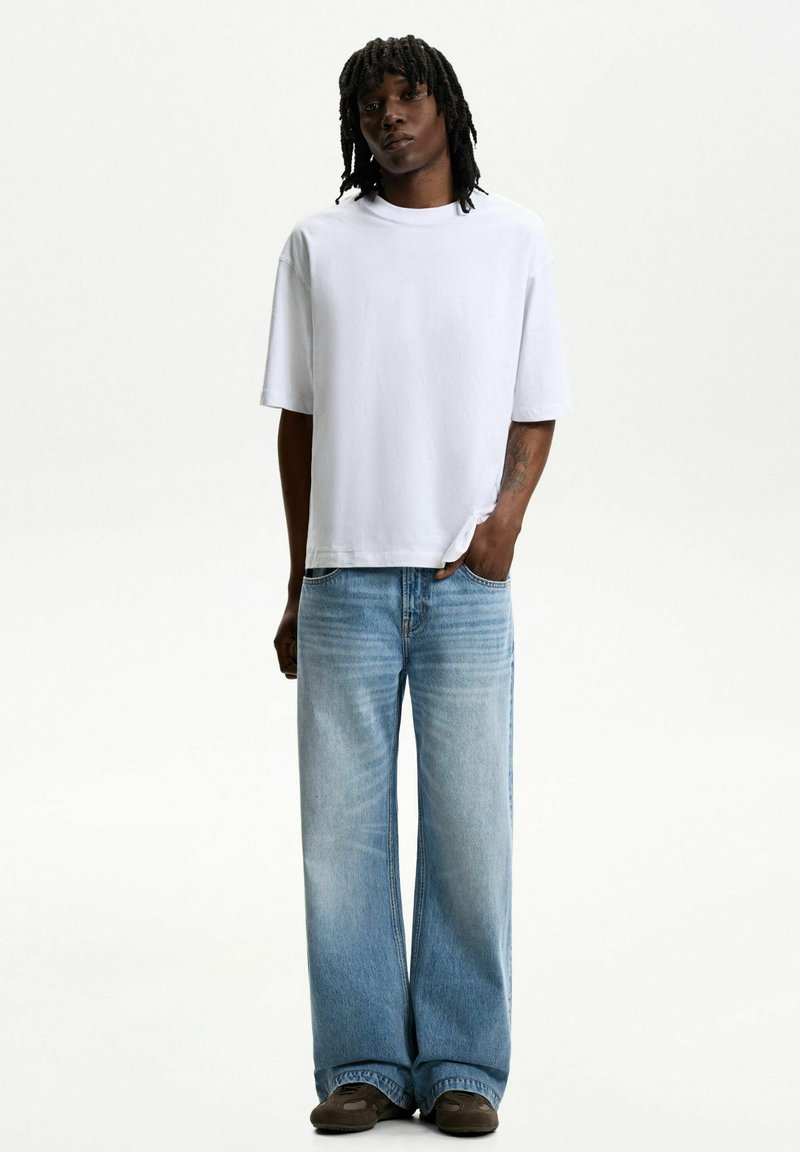 White short-sleeve t-shirt paired with light blue wide-leg denim jeans. The jeans feature a faded texture and classic five-pocket design.