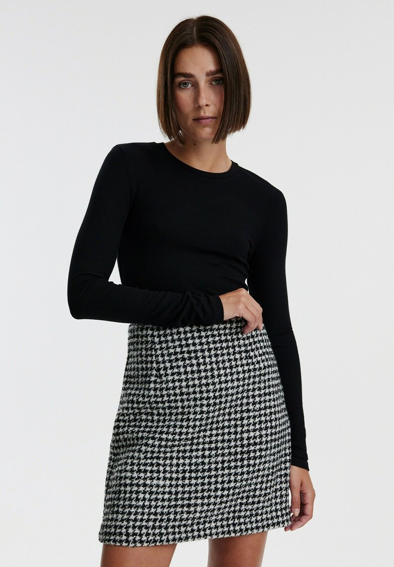 Zwarte langwerpige top gecombineerd met een zwart-wit houndstooth patroon mini-jurk, met een textuurstof en een aansluitend ontwerp.