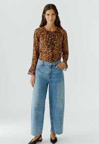 Bruine blouse met luipaardprint en een gerimpelde halslijn, gecombineerd met lichtblauwe spijkerbroeken met hoge taille en brede pijpen. Zwarte puntige ballerina's.