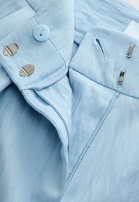 Világoskék nadrág derékrész, gombbal, két kampós kapoccsal és látható varrással texturált anyagon.