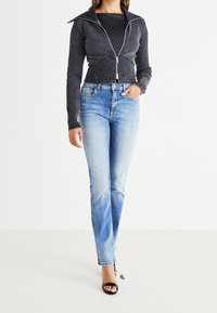 Zwarte cropped zip-up jacket met lange mouwen, gecombineerd met lichtblauwe vervaagde rechte jeans en zwarte bandjes sandaal.