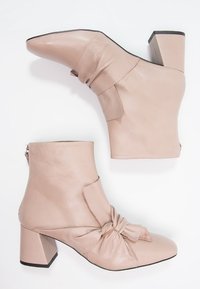 Taufärgad läderankelboots med en knuten frontdetalj, blockklack och siddragkedja. Slät textur och spetsig tådesign.