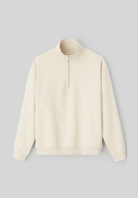 Pull beige clair, tissu doux, col montant avec fermeture éclair, manches longues, et bords côtelés au niveau des poignets et de l'ourlet. Design minimaliste, sans motifs.
