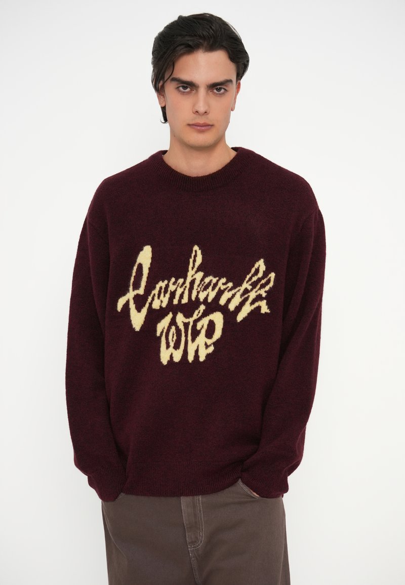 Bordeaux gebreide trui met een crème logo ontwerp, ronde hals en geribbelde mouwen. Zachte textuur met een relaxte pasvorm en lange mouwen.