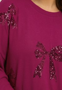 Pull en tricot fuchsia avec des motifs de nœuds en sequins sur les épaules, doté d'une texture douce et d'un col rond.