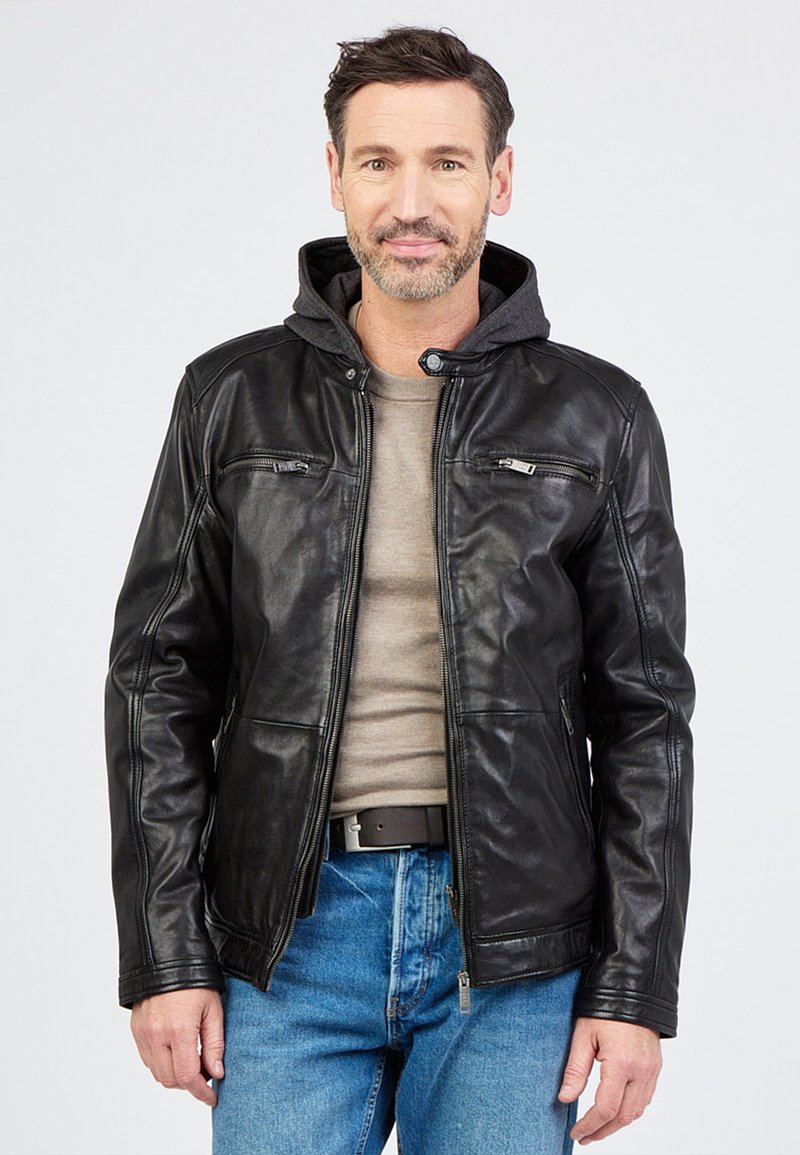 Sort læderjakke med grå hættetrøjeforing, lynlåslommer og tætsiddende design. Bæret over en beige skjorte og blå jeans.