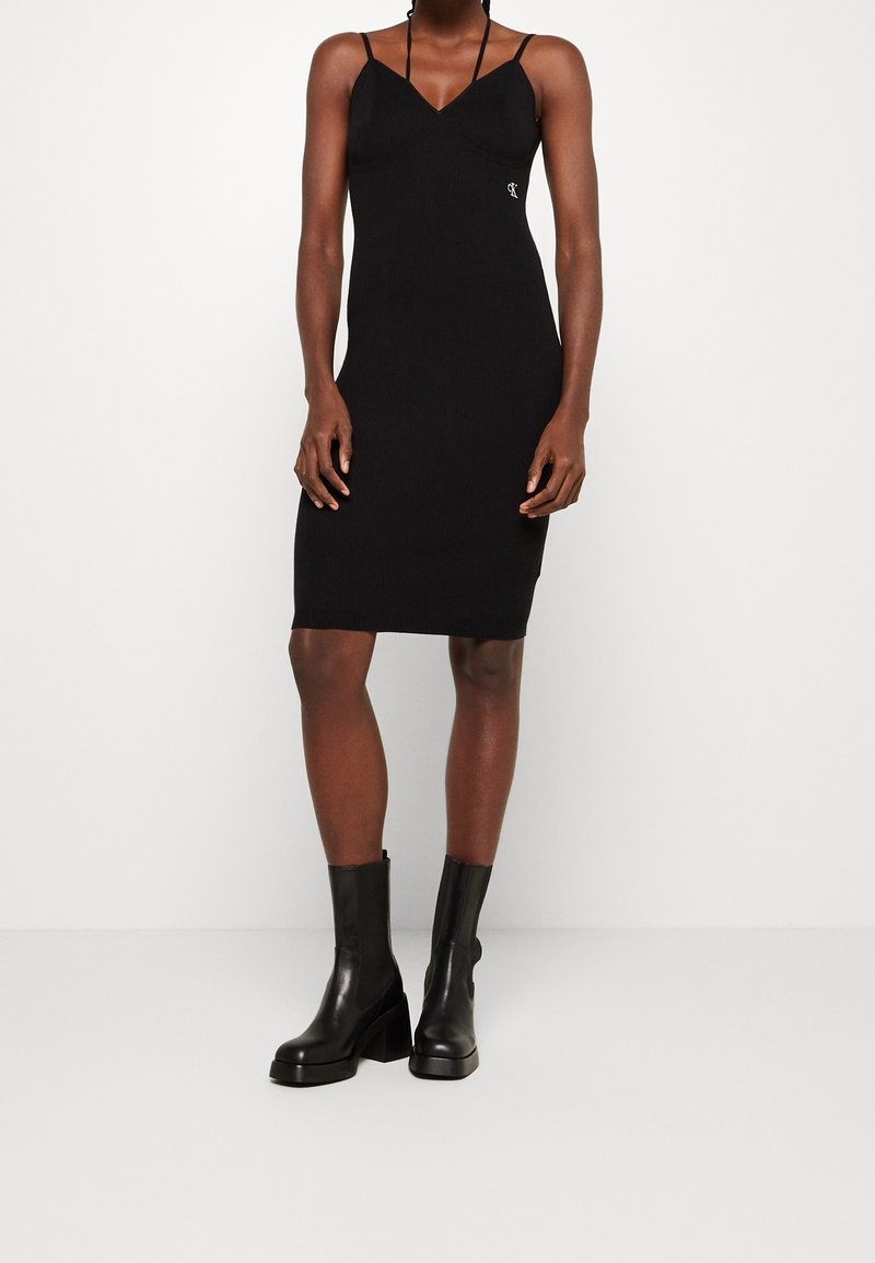 Svart ribbad klänning med tunna spaghettistroppar, en tight passform och v-ringning. Bärs med högklackade svarta läderankläder.