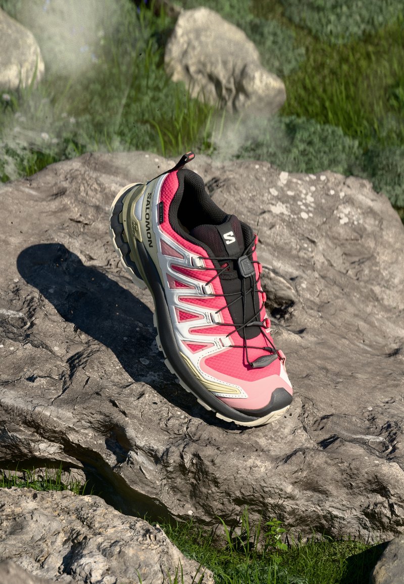 Trail running shoe in pink and black, featuring a synthetic upper, textured finish, lacing system, and a rugged outsole with a thick sole.