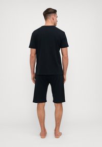 Camiseta de algodón negra con mangas cortas y pantalones cortos negros, con un diseño simple y un ajuste relajado. Sin patrones ni acentos visibles.