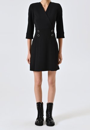 Woman wearing a black wrap dress with three-quarter sleeves and silver button details, paired with black lace-up combat boots.