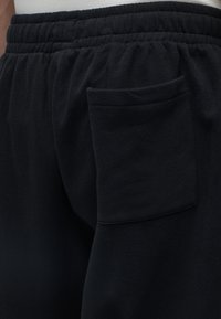 Κοντινό πλάνο μαύρου παντελονιού fleece με ελαστική μέση και τετράγωνη τσέπη στη δεξιά πλευρά.