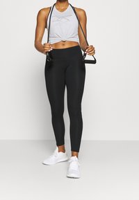 Ljusgrå krossad linne med en knuten detalj, matchad med svarta leggings och vita sportskor. Leggings har en subtil logodetalj.