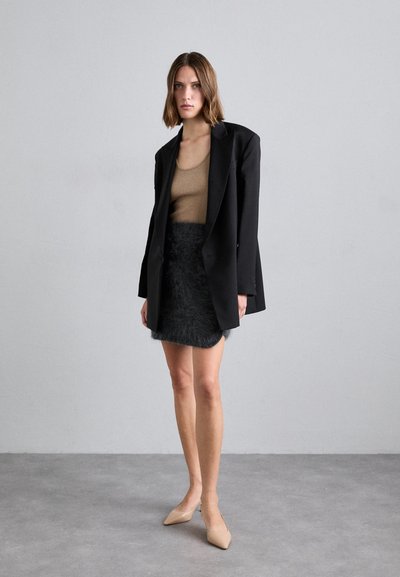 Sacou oversized negru, top ajustat bej și o fusta scurtă pufoasă neagră. Tacâmuri bej cu vârful ascuțit. Texturi netede și culori contrastante.