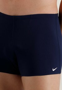 Sötétkék fürdőnadrág rugalmas anyagból, formázott kivitelben. Az alsó elülső részen fehér Nike logó található.