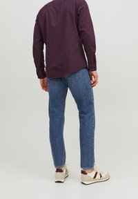 Mörkrutigt knapp-up skjorta, blå jeans och beige sneakers med röda detaljer, sedd bakifrån. Avslappnad passform och slitstarkt tyg.