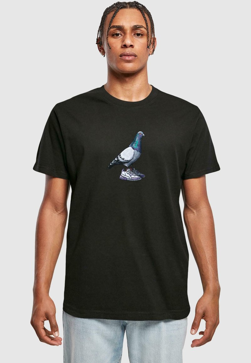 Sort bomuld t-shirt med et grafisk tryk af en due iført sneakers. Designet er centreret og farverigt med detaljerede fjer og sko.