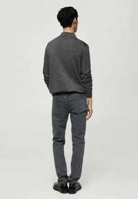 Grau gestrickter Pullover mit Kragen und strukturiertem Muster, kombiniert mit dunkelgrauen Jeans, von hinten betrachtet. Schwarze Schuhe vervollständigen den Look.
