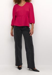 Fuchsiabluse med V-hals, samlet talje og trekvartærmer, parret med høj talje sorte bukser med bred ben og spidse sorte hæle.