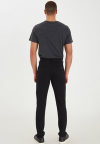 Schwarze Hose mit Slim-Fit, aus robustem Material gefertigt. Verfügt über zwei Gesäßtaschen und einen Bund mit Kordelzug. Kombiniert mit einem grauen T-Shirt.