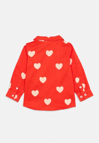 Chemise rouge à manches longues avec un motif de grands cœurs crème, poignets à bouton, col et ourlet arrondi. Fabriquée en tissu de coton.
