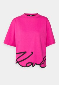 Rosa Baumwoll-T-Shirt mit Rundhalsausschnitt, kurzen Ärmeln und einem schwarzen, geschwungenen Logo-Design am Saum. Weicher Stoff und kurzer Schnitt.
