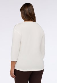 Maglietta a maniche lunghe color crema realizzata in tessuto morbido, con scollo rotondo e orlo curvo, caratterizzata da leggere rifiniture sulle spalle.