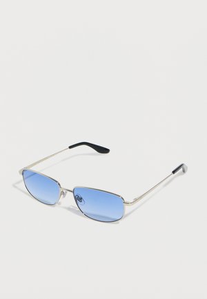 Occhiali da sole rettangolari con montatura in metallo, lenti sfumate blu e terminali delle aste neri su una superficie bianca.