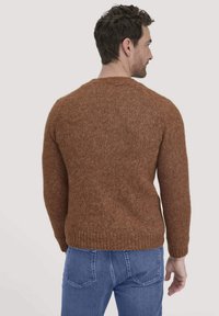 Brauner Strickpullover mit strukturiertem Finish, featuring einen Rundhalsausschnitt, geripptem Saum und Design mit abgesenkten Schultern. Getragen mit blauen Jeans.
