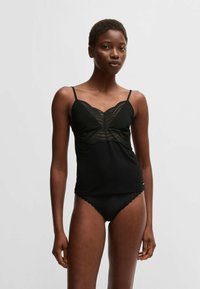 Czarny top na ramiączkach z koronkowym wykończeniem przy biuście, cienkimi ramiączkami i dopasowanym krojem. W zestawie z pasującą czarną bielizną wykończoną koronką.