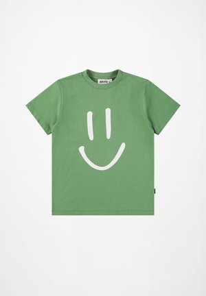 Πράσινο βαμβακερό μπλουζάκι με μεγάλη λευκή γραφική παράσταση ενός χαμογελαστού προσώπου στο μπροστινό μέρος. Σχεδίαση με κοντά μανίκια και στρογγυλή λαιμόκοψη. Το ταγκ είναι ορατό στη πλευρά.