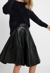 Svart fluffig tröja med långa ärmar, matchad med en svart läderkjol i midi-längd med en utsvängd design och horisontella sömdetaljer.