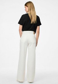 Platām kājām baltas bikses ar divām aizmugures kabatām un augstu jostasvietu, apvienotas ar īsu melnu t-kreklu. Gluda auduma ar nelielu spīdumu.