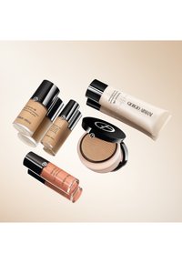 Fem Giorgio Armani skjønnhetsprodukter: to foundationflasker (beige), en fuktighetsgivende primer (uklar), en puddercompact (svart lokk, gylden pudder) og en glans (rose).