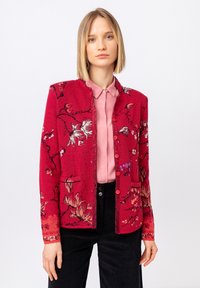 Rdeč cvetlični cardigan z teksturiranim zaključkom, ki ima zapletene cvetne vzorce, okroglo izreznico in gumbno zapiranje. Usklajen z roza bluzo.