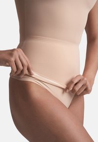 Béžové stahovací prádlo s hladkou, elastickou texturou, vysokým pasem a flexibilním pasem, který je upravován rukou.