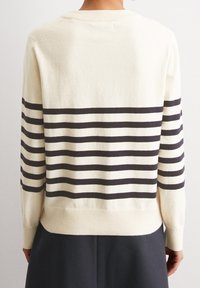 Maglione crema con strisce orizzontali nere. Polsini e orlo a costine, texture morbida. Vestibilità casual e rilassata, con scollo rotondo e spalle drop.