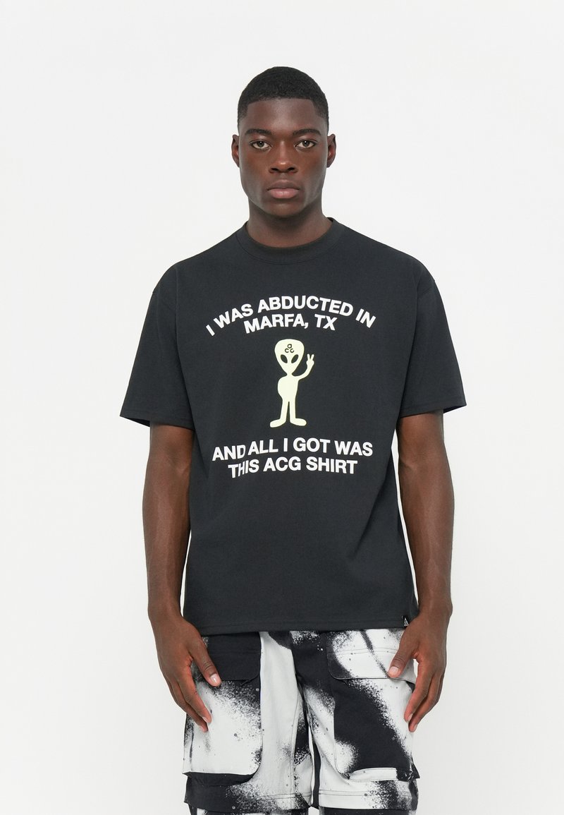 Svart bomulls t-shirt med vit text som lyder: "JAG BLEV ABDUCERAD I MARFA, TX OCH ALLT JAG FICK VAR DENNA ACG TRÖJA."
