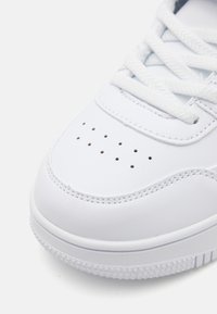 Valkoiset tennarit, joissa on sileä synteettinen päällinen, rei'itetty kärki, teksturoitu nauha ja kumipohja, jossa on tähden kuvio.