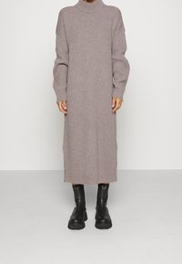 Lång, ribbad, mauve klänning med hög krage och sänkta axlar. Bärs med svarta ankelboots med tjock sula och ringdetaljer.