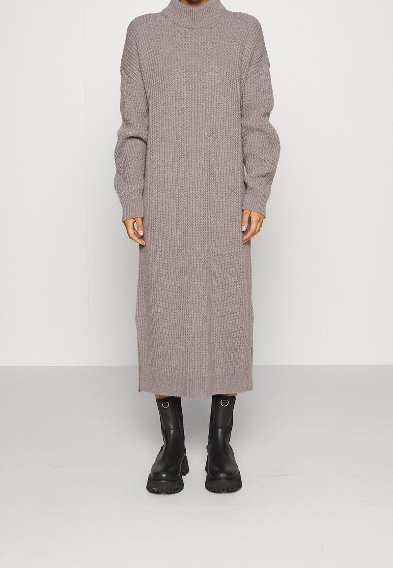Lång, ribbad, mauve klänning med hög krage och sänkta axlar. Bärs med svarta ankelboots med tjock sula och ringdetaljer.