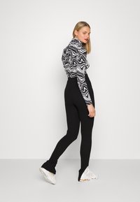 Black ribbed leggings with split hems, paired with a black and white abstract patterned turtleneck and white sneakers.