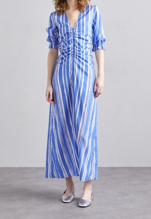Woman wearing a blue and white vertically striped midi dress with ruched front and puffed elbow-length sleeves, paired with silver flats.
