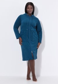 Robe cappuccio teal realizzato in materiale morbido, con chiusura a zip, due tasche frontali e uno spacco frontale per facilitare i movimenti.