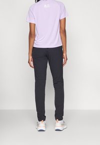 Lila krátká košile s krátkými rukávy a logem na zádech, v kombinaci s černými kalhotami a vícebarevnými sportovními botami, pohled zezadu.