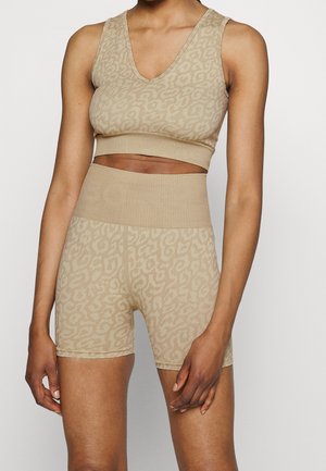 Mujer con top corto sin mangas beige a juego y pantalones cortos de talle alto con un sutil estampado de leopardo.