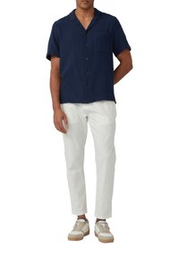 Marineblaues kurzärmeliges Hemd mit Knöpfen und einer Tasche, kombiniert mit weißen Hosen und neutralen Sneakers mit cremefarbenen und beige Akzenten.