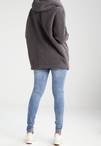 Giacca in pile grigia e morbida con cappuccio, abbinata a jeans skinny blu chiaro e sneaker bianche. Tessuto notevole e vestibilità rilassata.